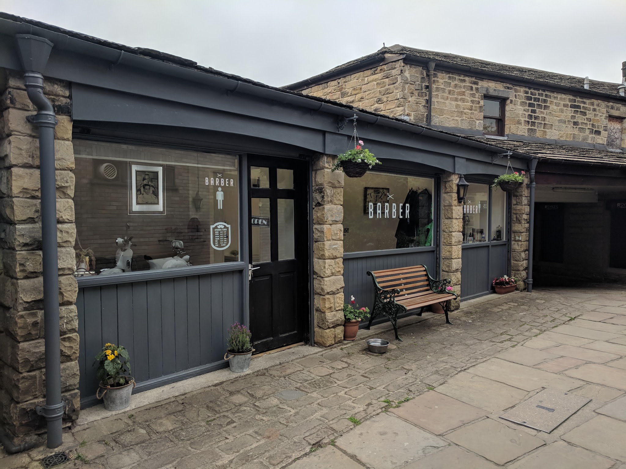 Courtyard Barber Shop's stone shopfront, dark woodwork and bench in New Market, Otley